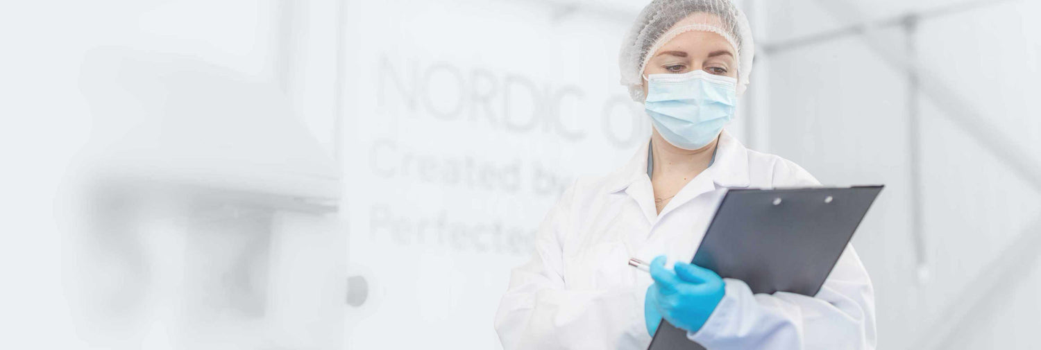 Un tecnico di laboratorio è lì in piedi, in abbigliamento protettivo, e scrive qualcosa sulla sua cartellina. 