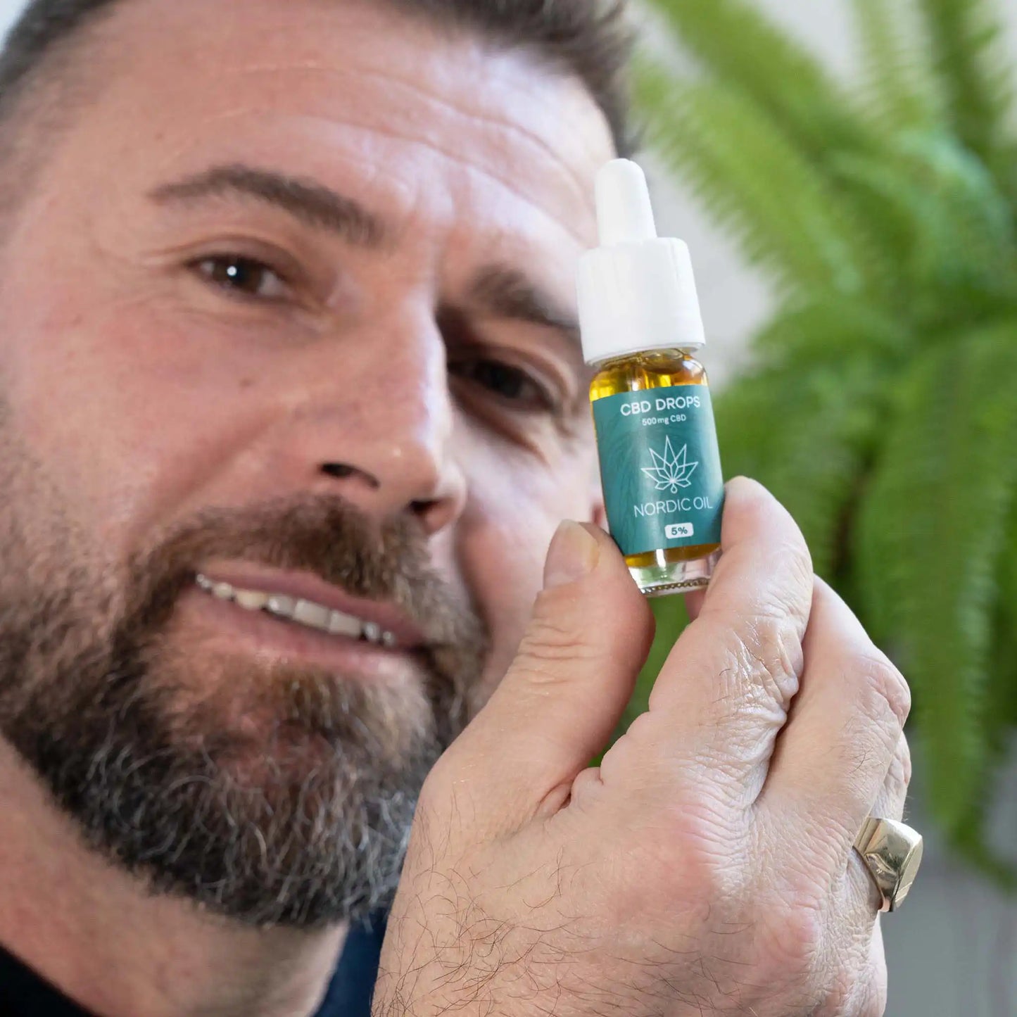 un uomo che sorride e tiene in mano l'olio di CBD per la telecamera