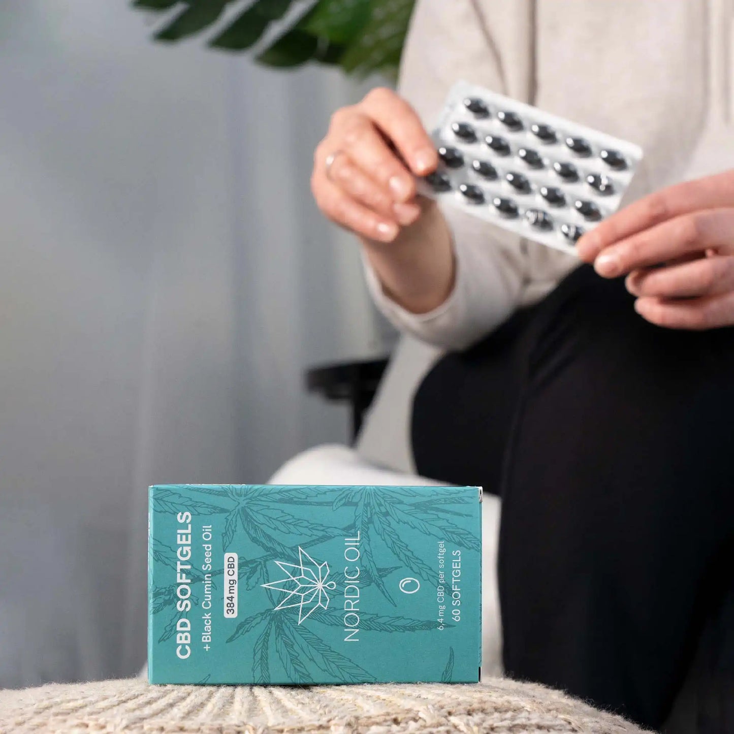 In primo piano, la confezione delle capsule di CBD; sullo sfondo, il cliente tiene le capsule.