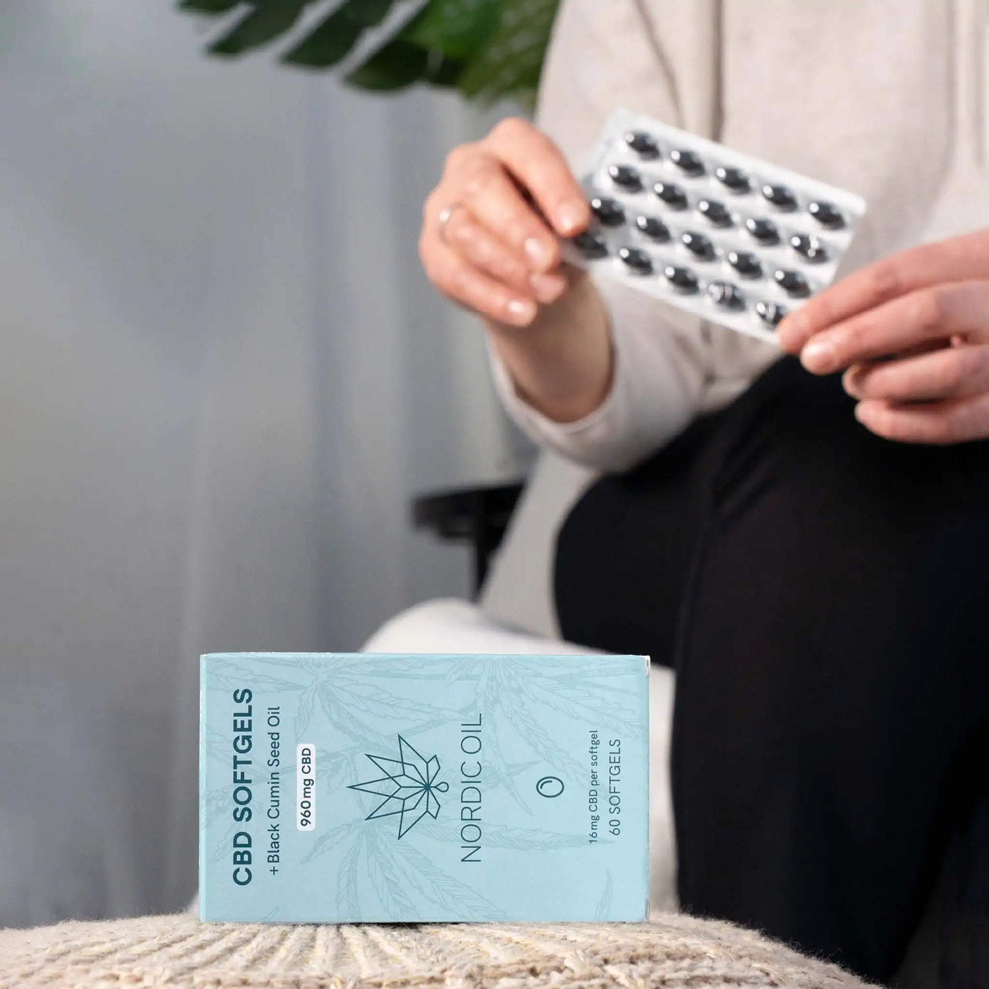 In primo piano, la confezione delle capsule di CBD; sullo sfondo, il cliente tiene le capsule.