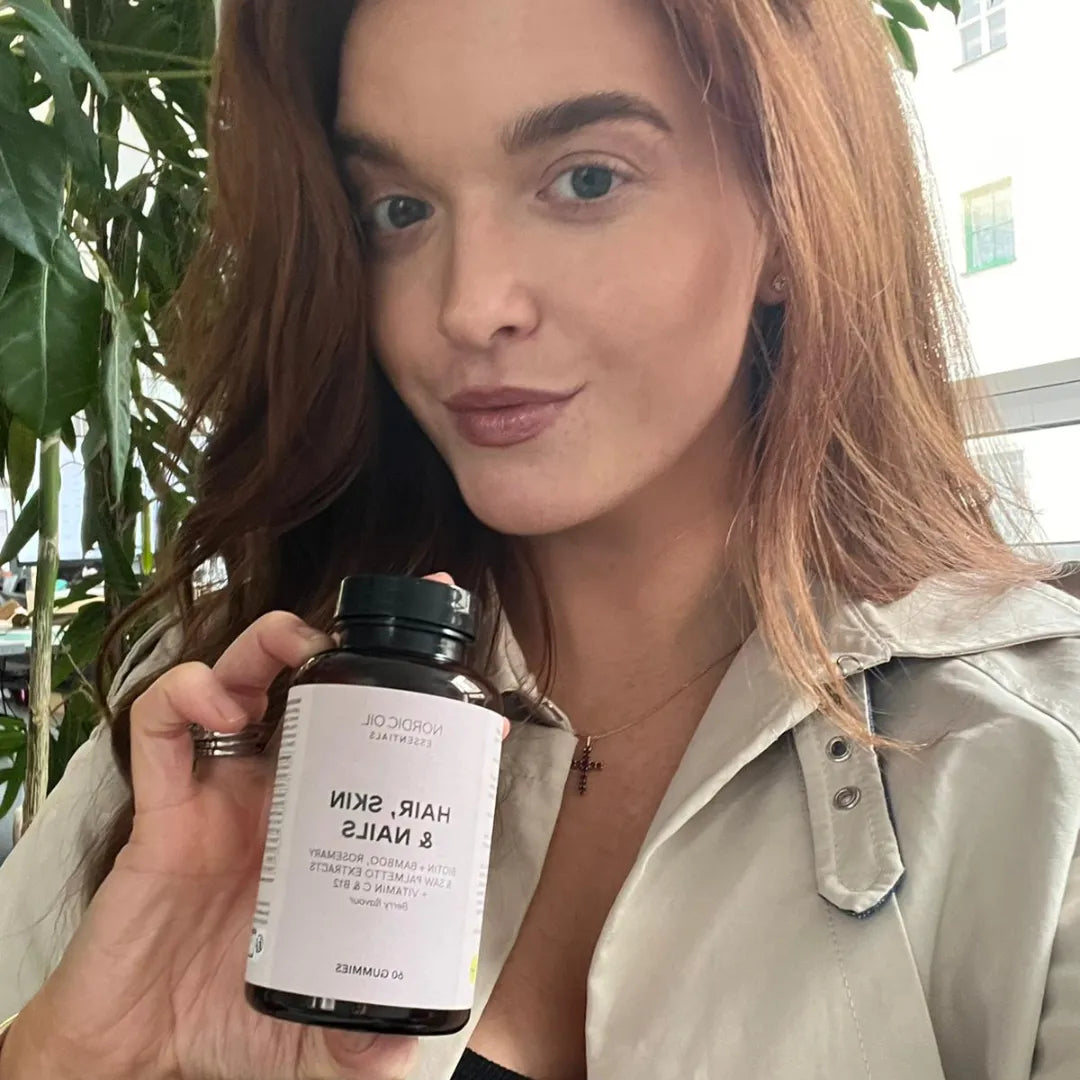 Donna con capelli castani chiari che tiene una bottiglia di integratore Hair Skin & Nails Nordicoil Essentials